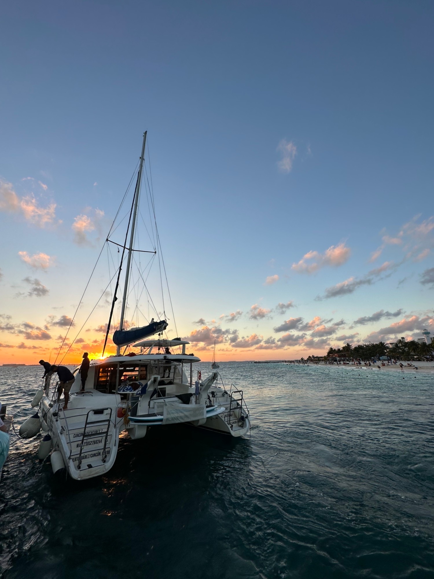 A catamaran moored at sunset with the sun setting behind its mast